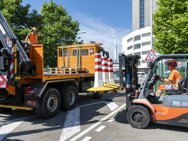 Arbeiter in Baufarzeugen laden Betonelemente auf zum Wegtransport.