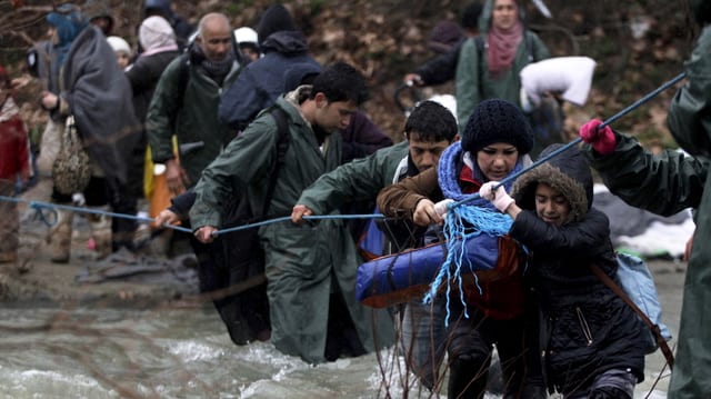 Flüchtlinge durchqueren einen Fluss und halten sich an einem Seil.