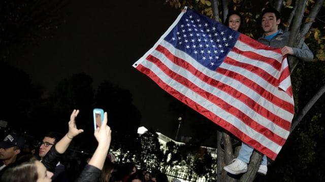 Junge Menschen in einem Baum vor dem Weissen Haus mit einer US-Flagge.