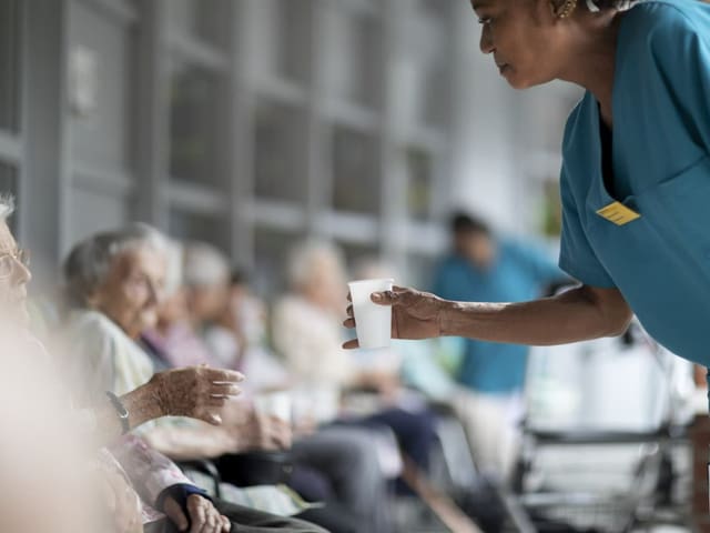 Pflegerin versorgt Altenheimbewohnerin mit Wasser