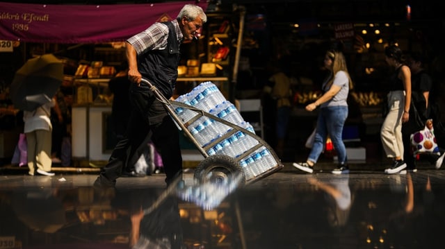 Ein Mann in Istanbul schiebt einen Wagen mit Wasser vor sich heran.