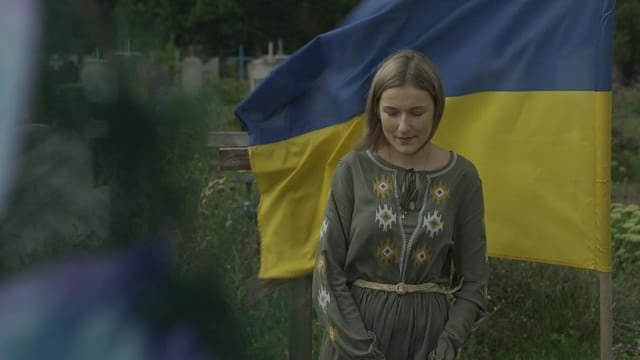 Junge Frau an einem Grab, im Hintergrund die ukrainische Flagge