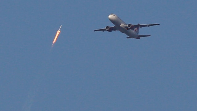 Rakete fliegt in den Himmel, Flugzeug daneben.