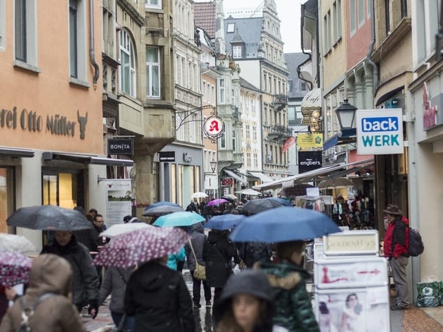 Menschen mit Regenschirmen in belebter Einkaufsstrasse.