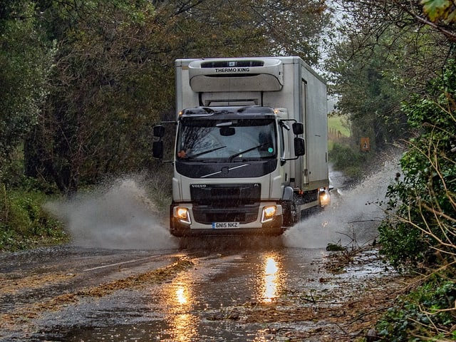 Ein LKW fährt auf einer überschwemmten Strasse. Auf den Seiten liegen überall heruntergefallene Äste.