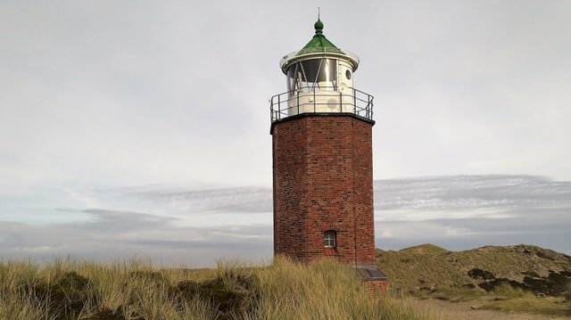 Ein rot beziegelter Leuchtturm an einem Strand bei rauem Wetter.