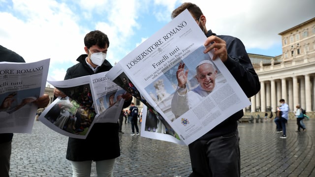 Two men stand up and read the newspaper.