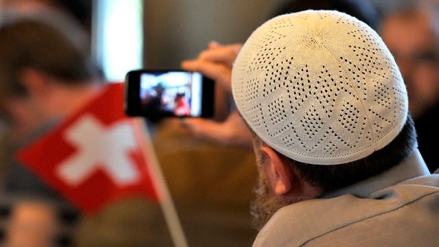 Ein Mann mit muslimischem Käppi schaut auf ein Smart Phone.