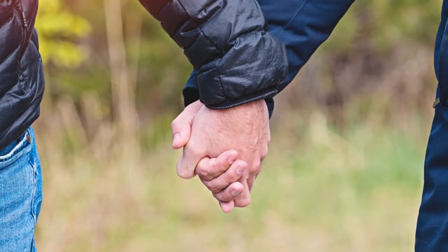 Zwei Männer halten Hände in Jacken.