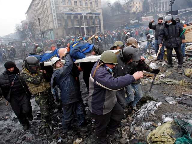 Behelmte Demonstranten tragen einen Verletzten auf einer improvisierten Bahre über den Maidan.