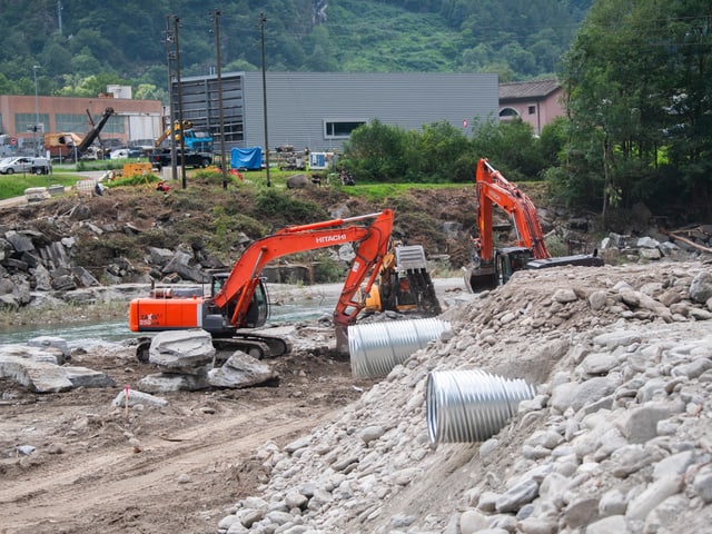 Zwei orange Bagger bei Bauarbeiten an einem Fluss.