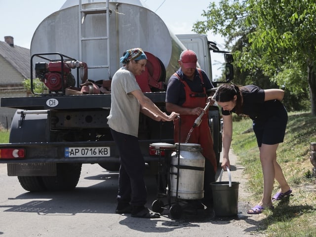 Lastwagen mit Wassertank. Davor stehen Menschen mit Wasserkübeln.