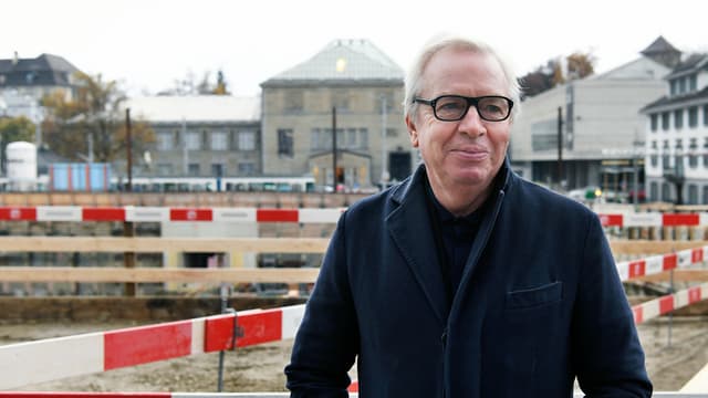 Ein Mann mit Brille steht vor einer riesigen Baustelle