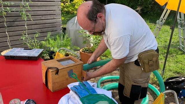 Mann hält grünen Schlauch, der an Holzkiste befestigt ist.