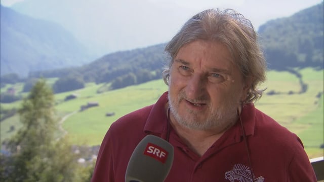 Mann spricht vor Bergkulisse ins Mikrofon