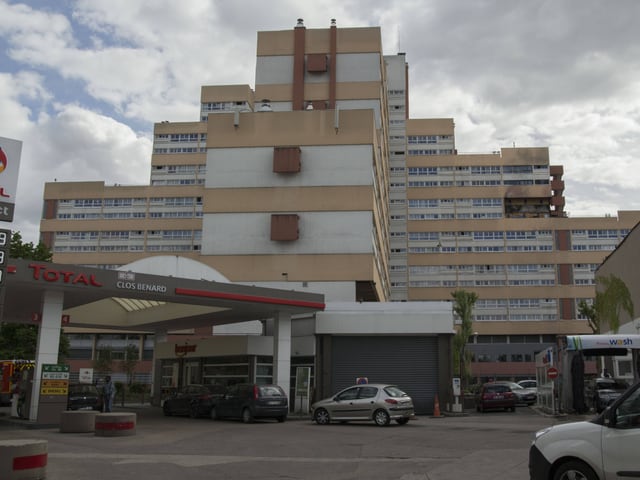 Total-Tankstelle im Vordergrund mit Hochhaus im Hintergrund unter bewölktem Himmel.