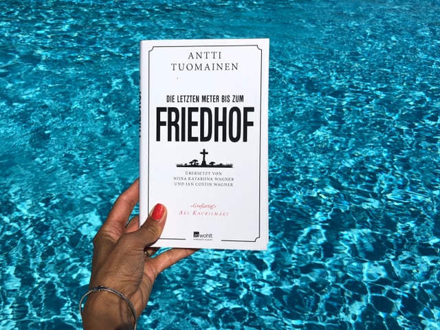 Annette König hält das Buch von Antti Tuomainen: «Die letzten Meter bis zum Friedhof» vor blaues Wasser