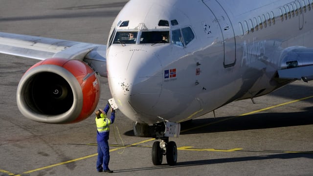 Ein Flugzeug am Boden, ein Techniker öffnet eine Klappe beim Bug.