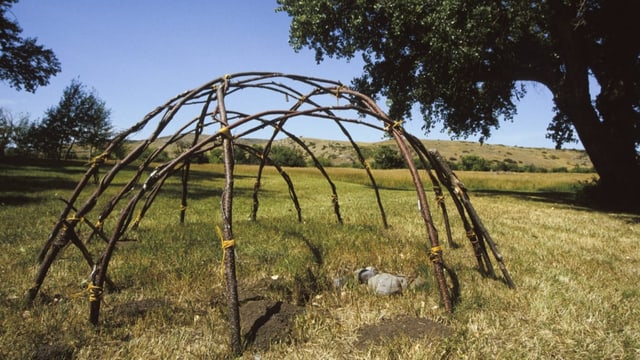 Auf einer sonnigen Wiese steht das Grundgerüst einer Schwitzhütte 