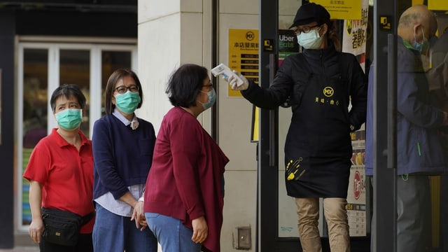 One woman measures the fever in another woman, all with masks.