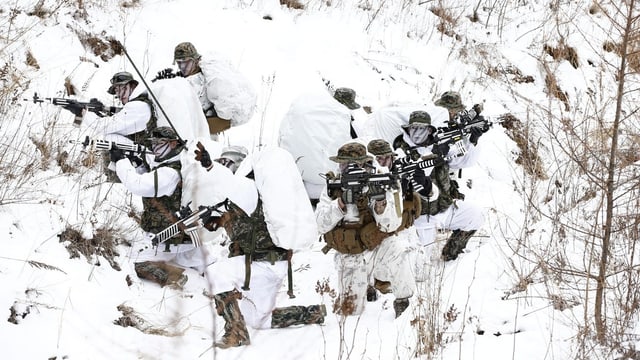 Soldaten in weissen Tarnanzügen operieren bewaffnet im Schnee.