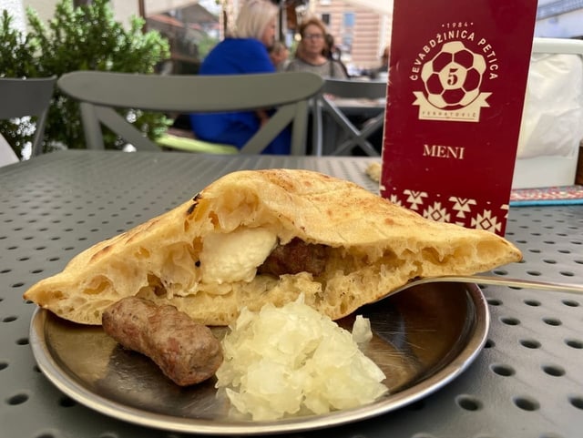 Fladenbrot, Cevapi und Zwiebeln liegen auf einem Teller.