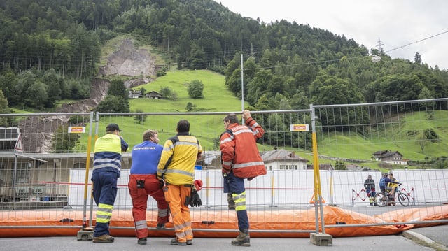 Drei Menschen schauen auf die Erdrutschstelle