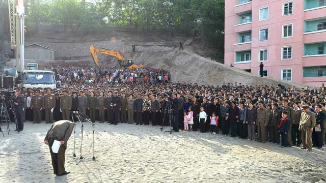 Koreanisches Behördenmitglied verneigt sich vor einer Menschenmenge in Norkorea.