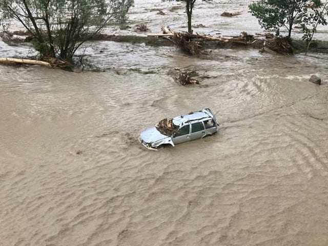 Ein Auto schwimmt im braun gefärbten Wasser, das bis zu dessen Scheiben hervorragt.