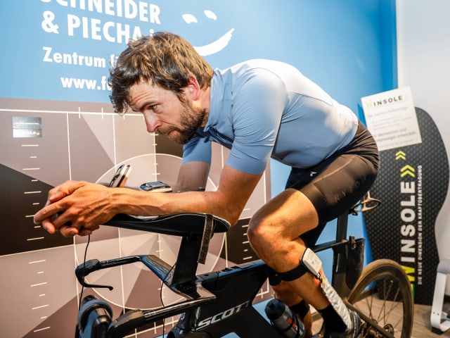 Mann in Radrennausrüstung auf einem stationären Fahrrad in einer Ausstellungshalle