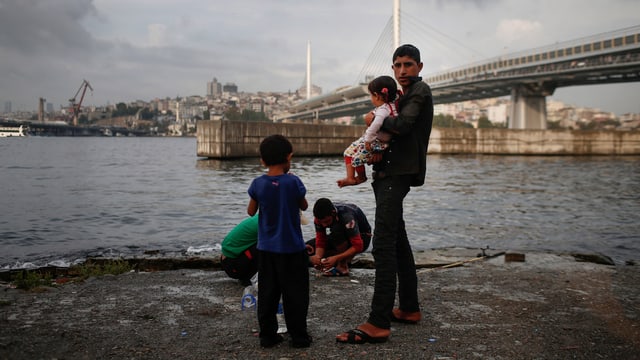 Ein syrischer Flüchtling steht mit seinen Kindern vor einer Brücke in Istanbul