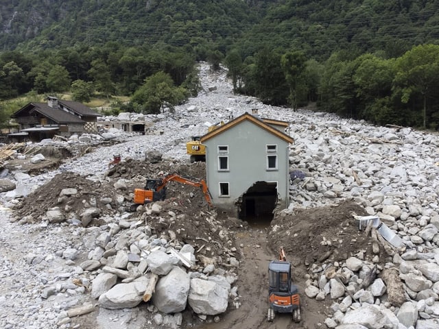 Ein einzelnes Haus steht in einer Gerölllawine neben zwei Baggern.