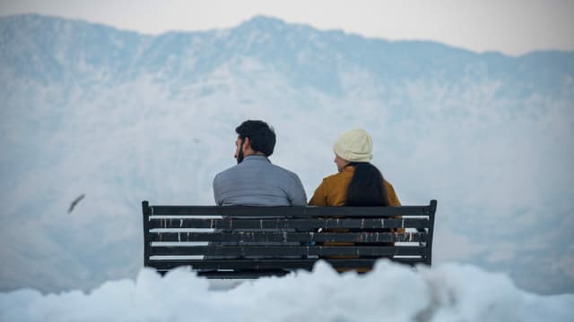 Ein Paar sitzt im Winter auf einer Bank mit schneeweissen Bergen im Hintergrund