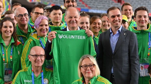 Eine Gruppe von Personen, teils in grüner Sportkleidung, mittig Olaf Scholz und Philipp Lahm.