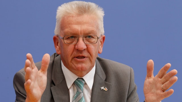 Kretschmann im Porträt vor blauem Hintergrund, mit den Händen gestikulierend.