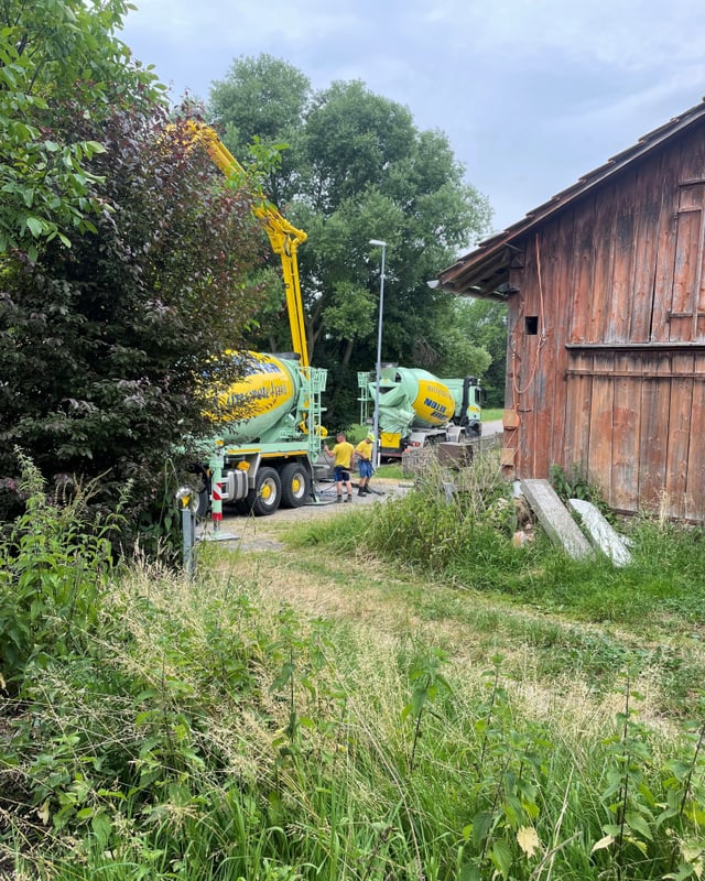 Auf dem Hinterhof des Bauernhauses. Zwei Arbeiter stehen neben Beton-Fahrmischer.