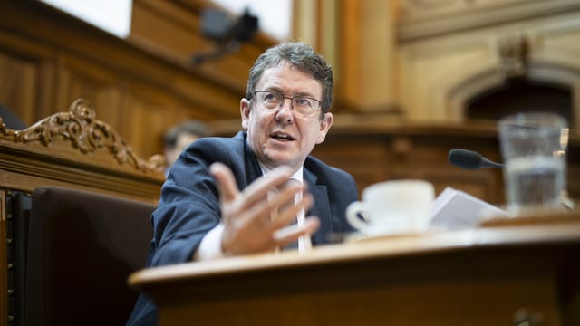 Ein Mann mit Brille in einem holzgetäferten Saal