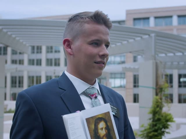 Ein junger Mann im Anzug mit einem geöffneten Buch im Freien.