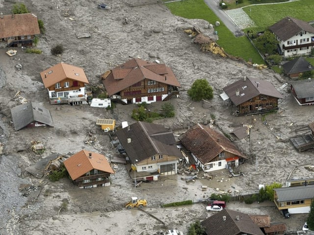 Viel Schutt, Geröll und Schlamm liegt mitten in einem Dorf, wo Häuser stehen.