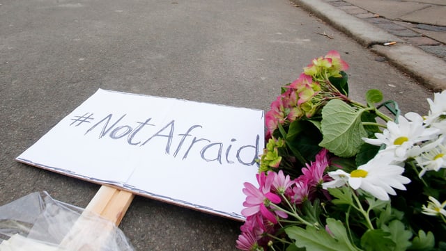 Ein Bild mit der Aufschrift «Not Afraid» liegt neben Blumen auf der Strasse.