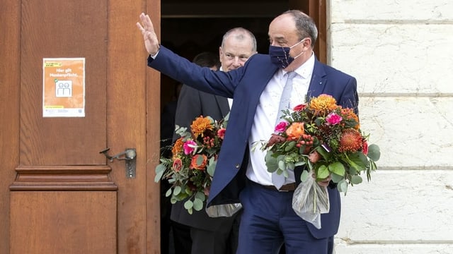 Markus Dieth with a bouquet of flowers, waving in front of the entrance door to the government building in Aarau.