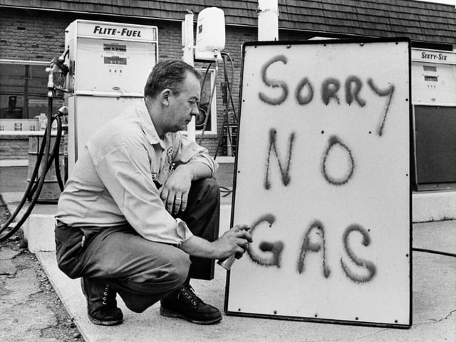 A man writes on a blackboard that he can no longer sell gasoline.