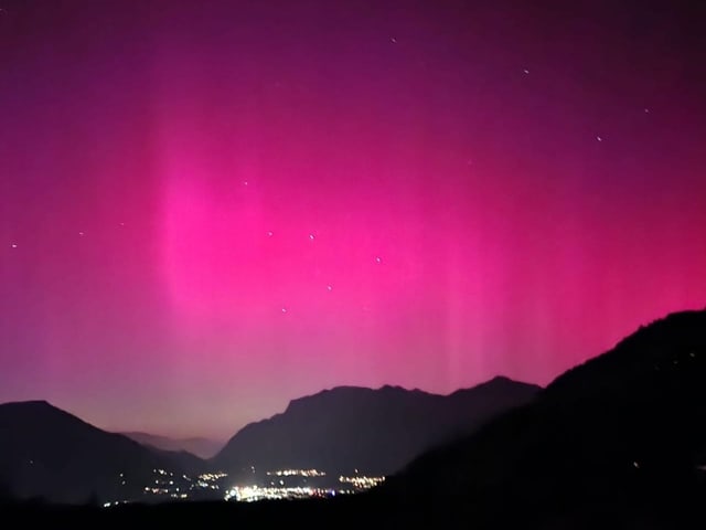 Rosaroter Himmel durch Polarlichter. Davor Silhouette der Landschaft.