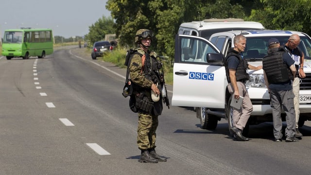 Soldat steht vor einem OSZE-Auto.