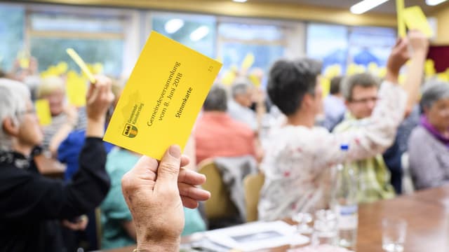 Teilnehmerinnen und Teilnehmer stimmen über ein Geschäft ab während einer Gemeindeversammlung in Kandersteg.