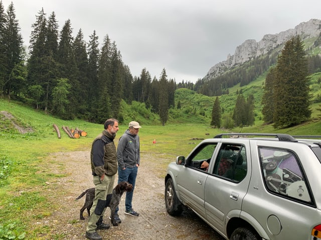 Zwei Männer stehen neben einem Auto und sprechen mit Person