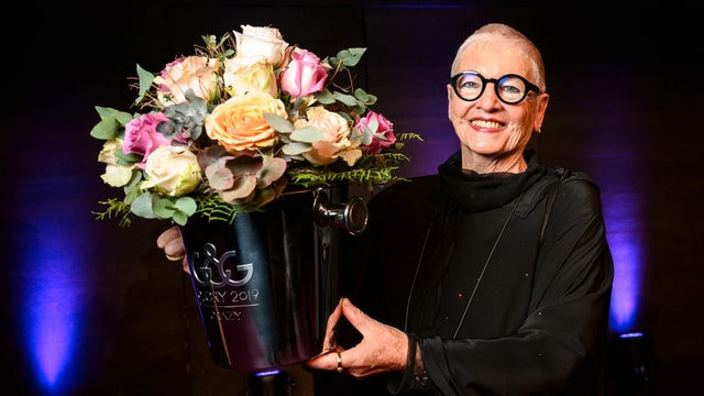 Frau in schwarzem Gewand mit Blumenstrauss in der rechten Hand