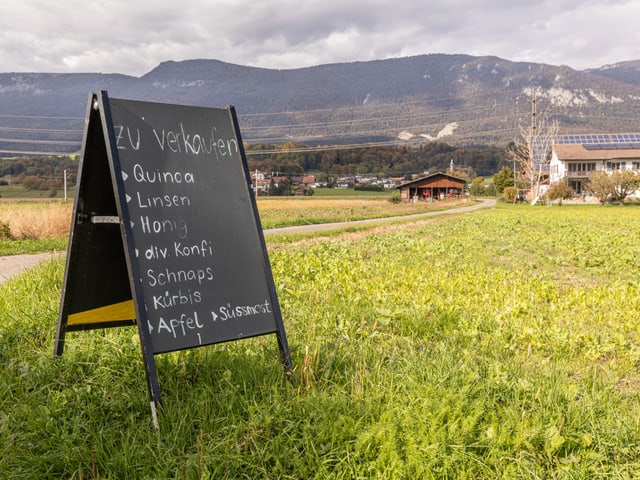 Tafel mit Verkaufsangeboten auf Feld vor Berglandschaft.