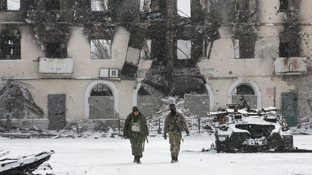 Kämpfer der selbsternannten Volksrepublik Donezk laufen an einem zerstörten Transporter der ukrainischen Armee vorbei. 