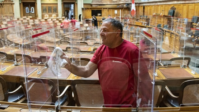 Mann in Arbeitskleidung putzt Plexiglasscheibe mit Tuch.